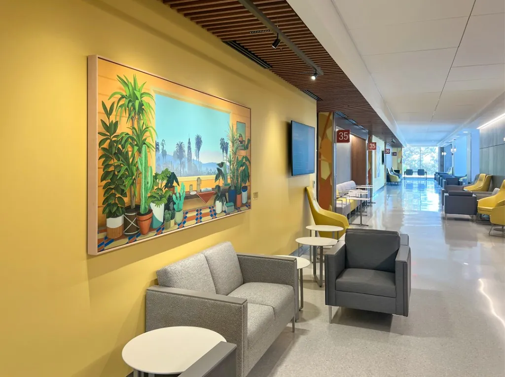 Framed Los Angeles cityscape-and-plants painting on a sunlit yellow wall at UC San Diego Health.