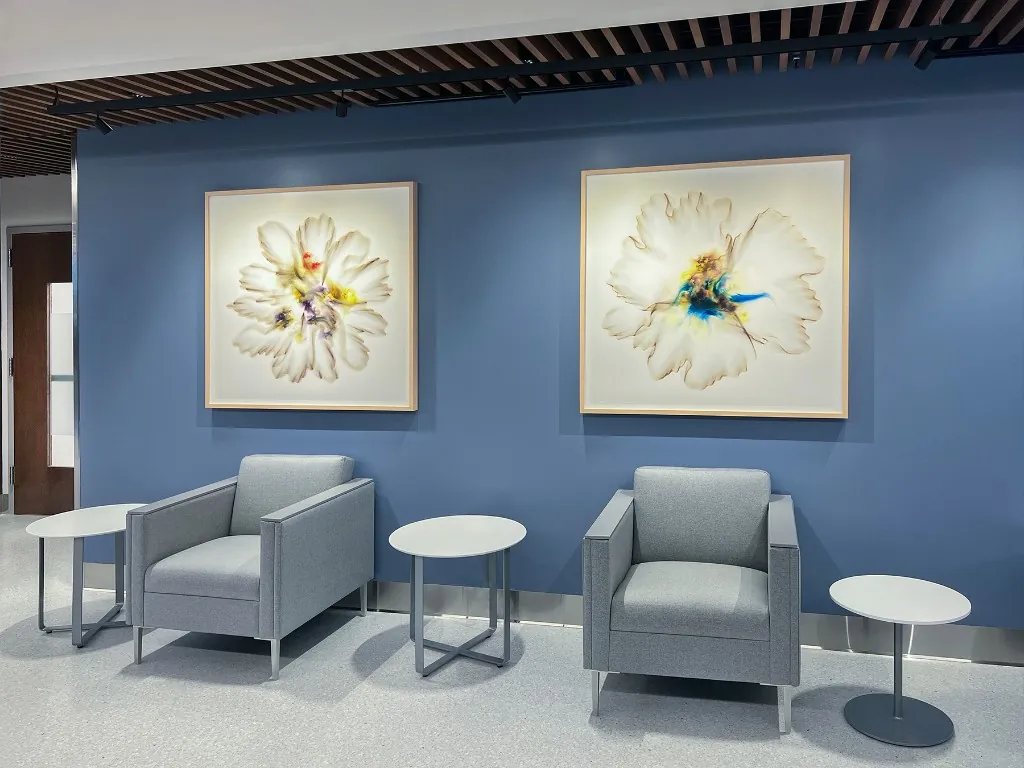 Two luminous large-scale floral works on a blue wall in a UC San Diego Health seating area.