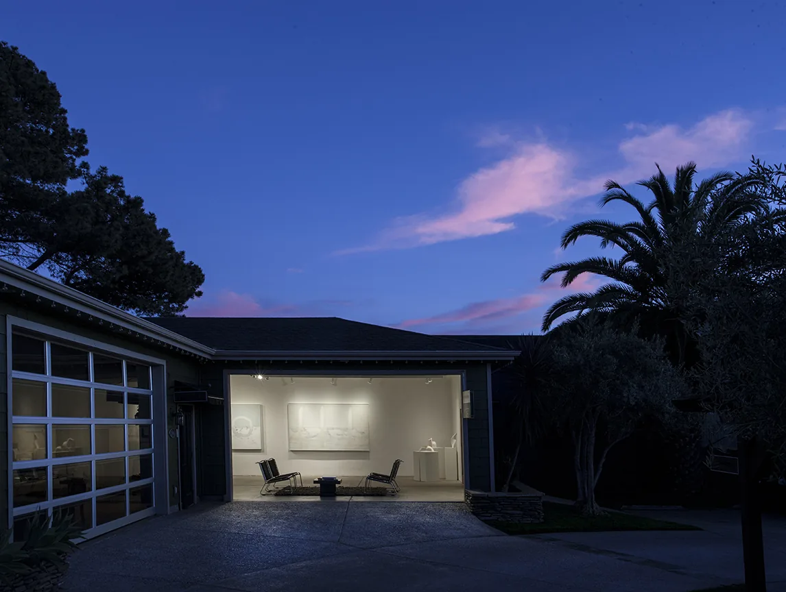 The Susan Street Fine Art gallery building at twilight, lit interior visible through the open front.